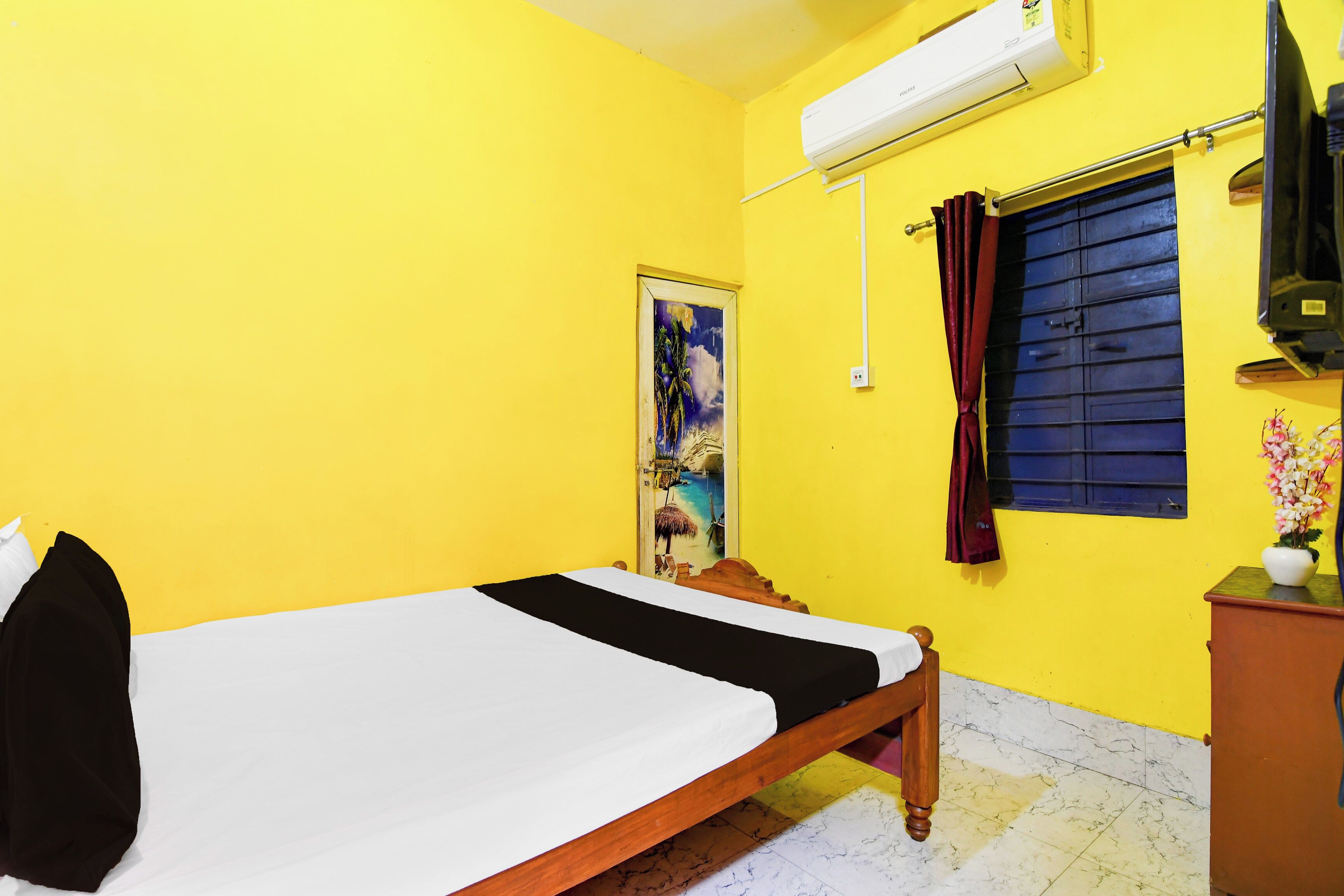 A room with a bed, a window with curtains, an air conditioning unit, and a wall-mounted television.