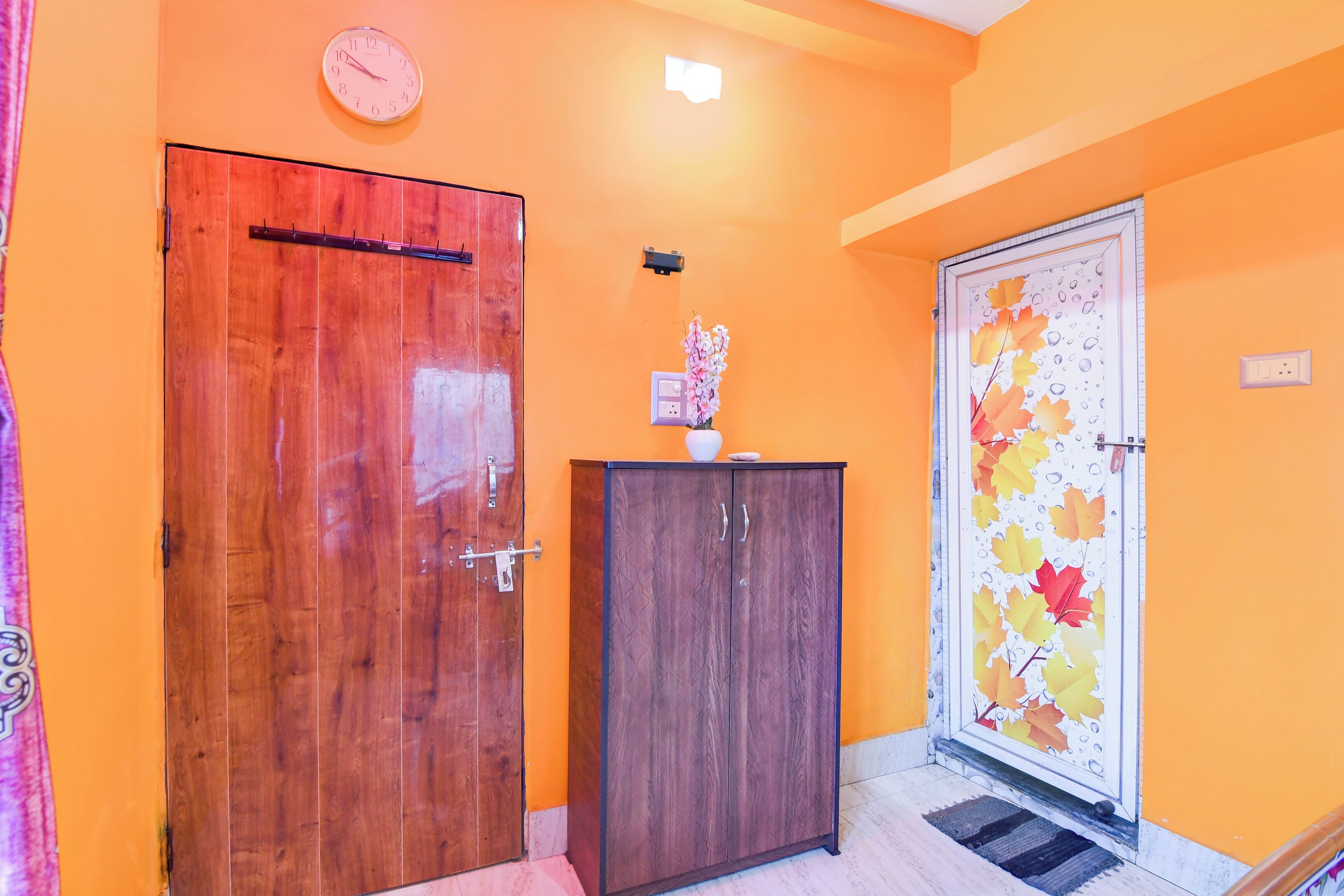 A hallway with two wooden doors, a clock on the wall, and a decorative door with autumn leaves.