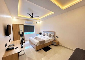 A modern bedroom with a bed, bedside table, desk, chair, and a ceiling fan. - Townhouse Highkey Boutique Hotel (Dhanbad)