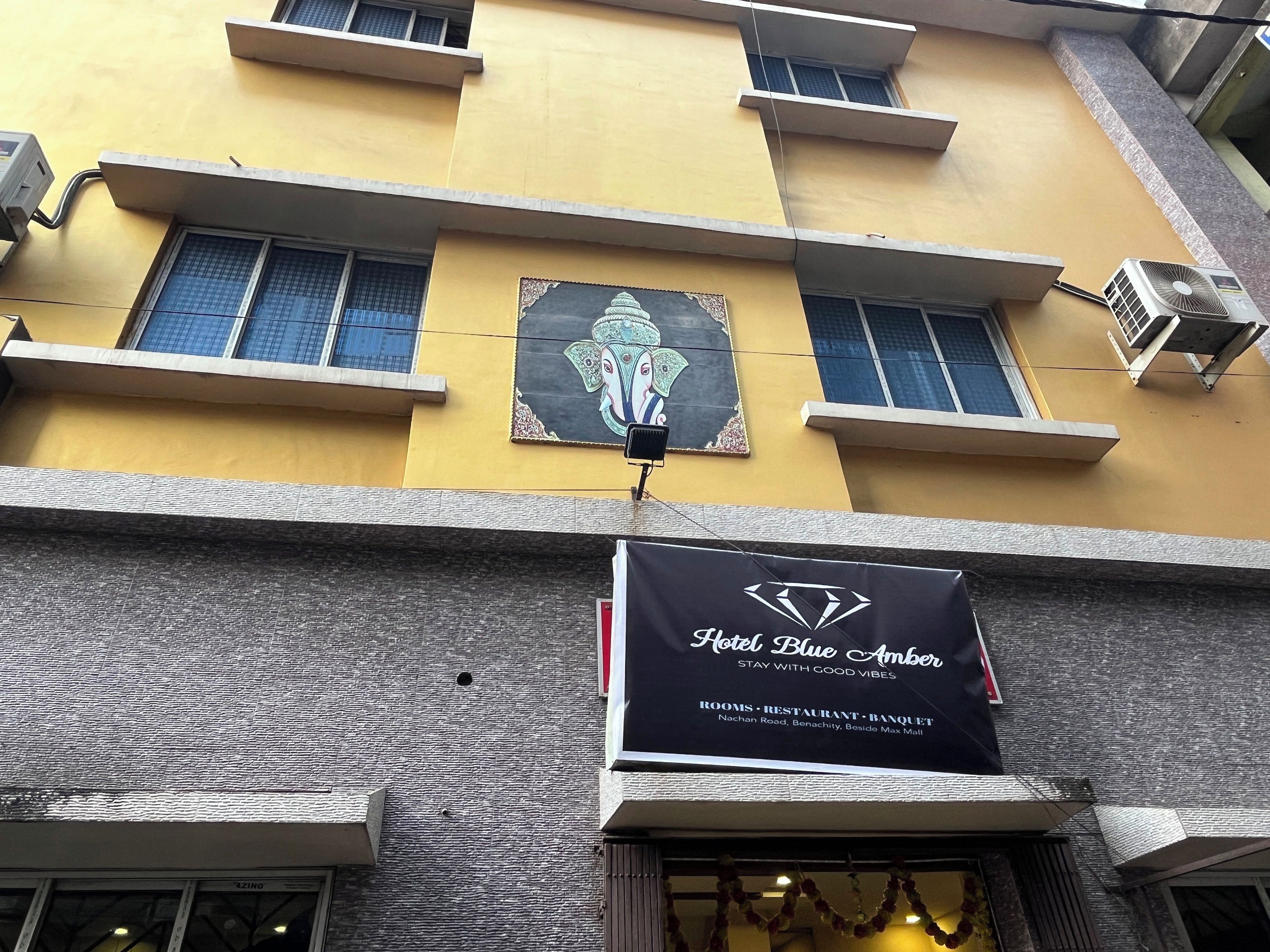 Un edificio con un cartel que indica Hotel Blue Amber, mostrando que ofrece habitaciones, un restaurante y un salón de banquetes.