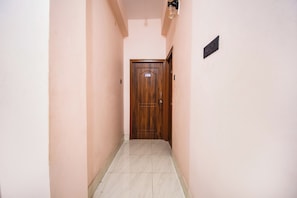 A narrow hallway with a wooden door at the end, a light fixture above, and a small sign on the wall.