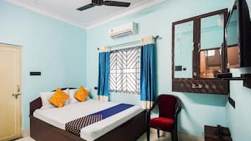 Un dormitorio con cama, una silla, ventilador de techo, equipo de aire acondicionado, ventana con cortinas y un espejo.