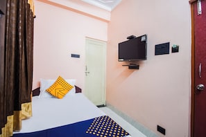 A hotel room with a bed, a television mounted on the wall, a door, and a wall socket.