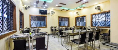A conference room with multiple tables and chairs, equipped with ceiling fans and a flat-screen TV.