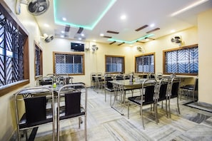 A conference room with multiple tables and chairs, equipped with ceiling fans and a flat-screen TV.