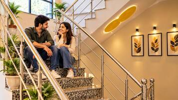 Um casal sentado em uma escada com design moderno, destacando um corrimão de metal e uma parede com obras de arte emolduradas.