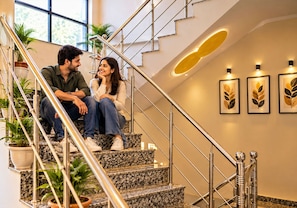Um casal sentado em uma escada com design moderno, destacando um corrimão de metal e uma parede com obras de arte emolduradas.