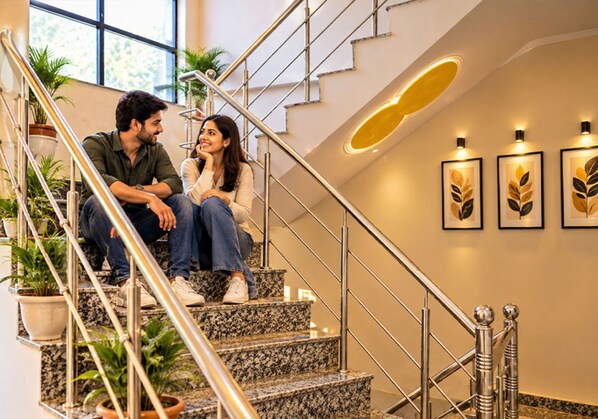 A couple sitting on a staircase with a modern design, featuring a metal railing and a wall with framed artwork.