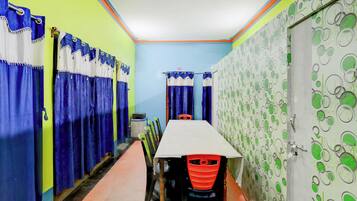 A hotel corridor with a row of rooms, a table with chairs, and a patterned wall.
