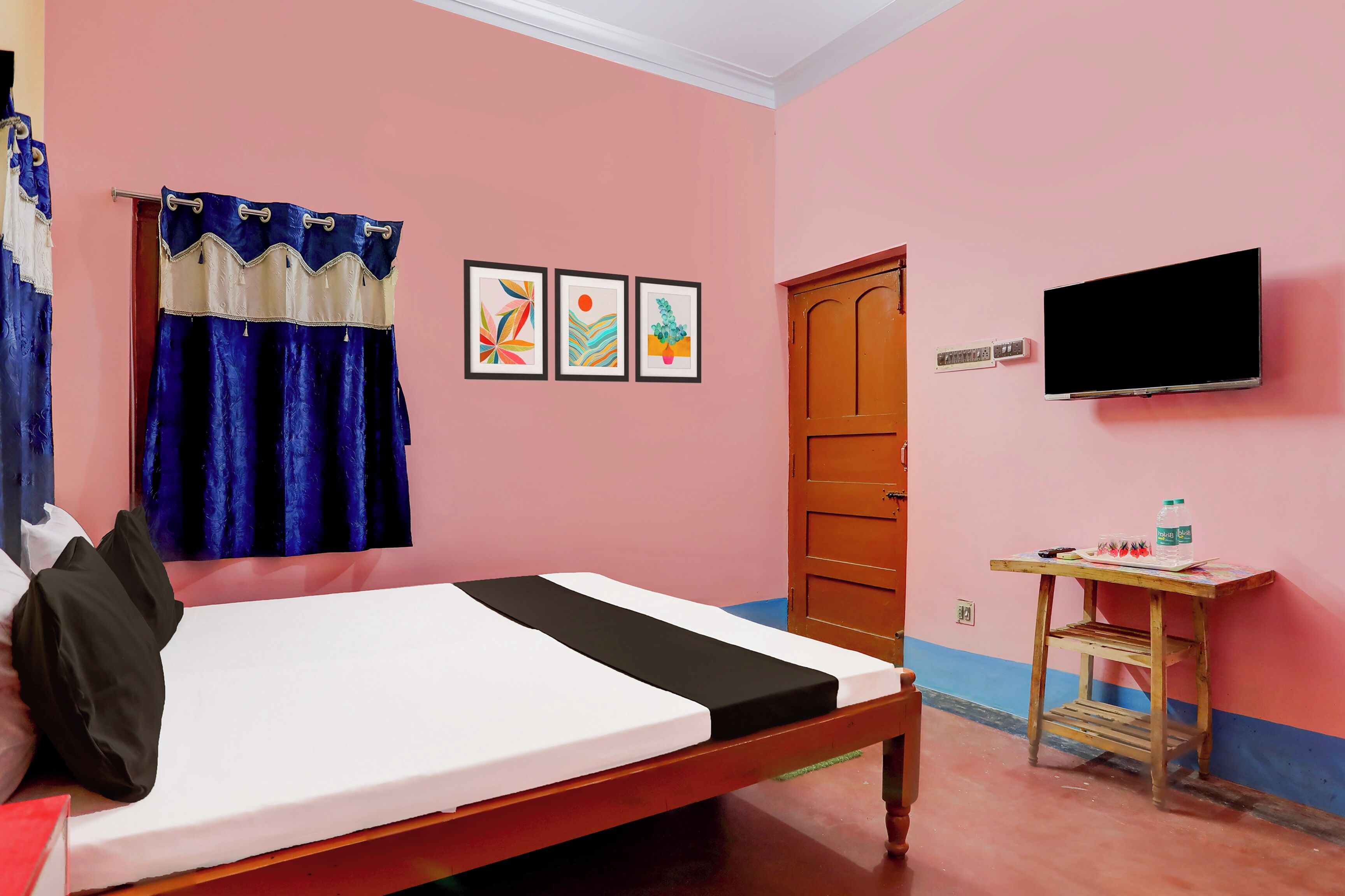 A room with a bed, a TV, a small table with a bottle, and a door.