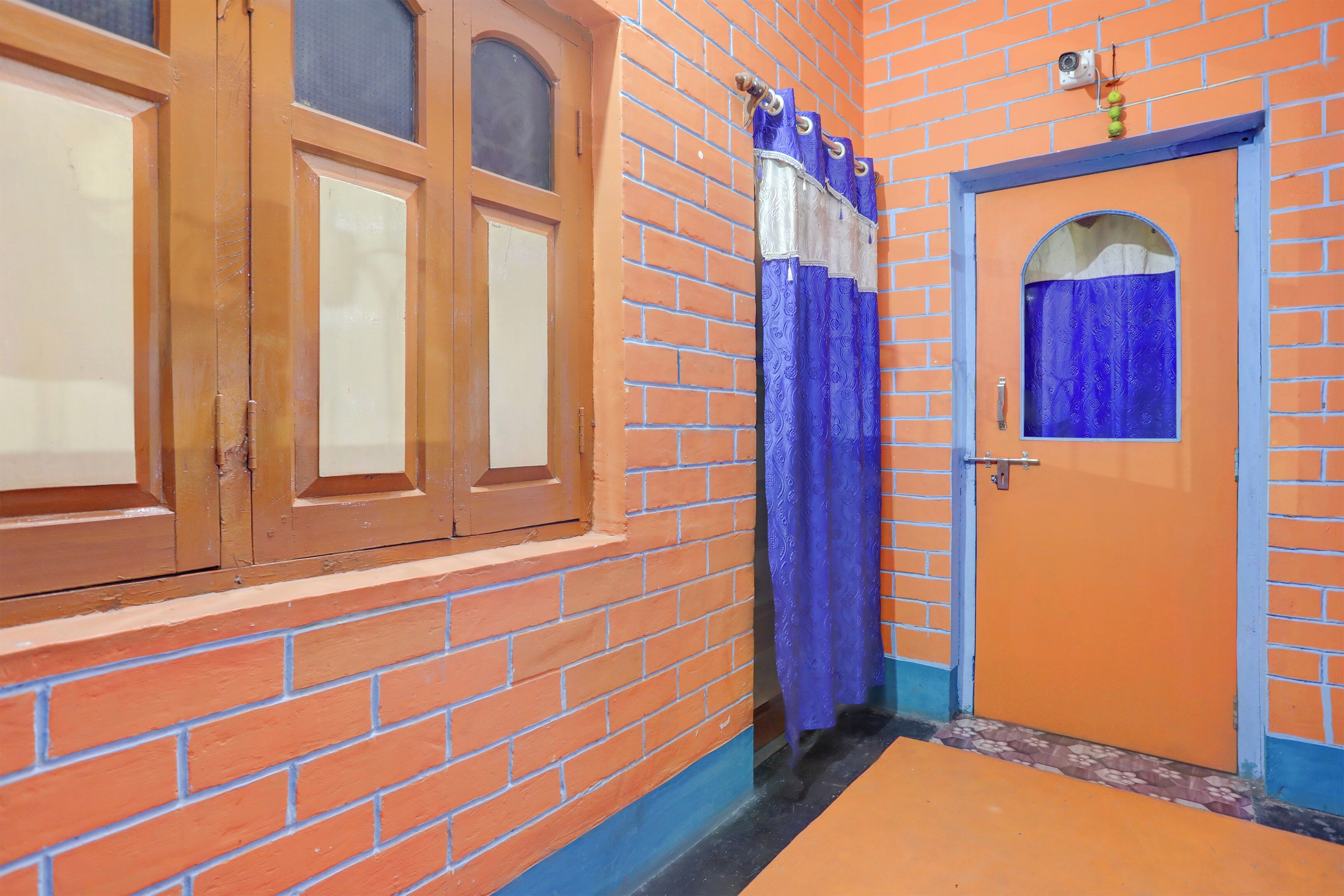 A corridor with a brick wall, a wooden door with a window, and a blue curtain.
