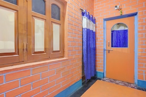 Un pasillo con pared de ladrillo, una puerta de madera con ventanal y una cortina azul.