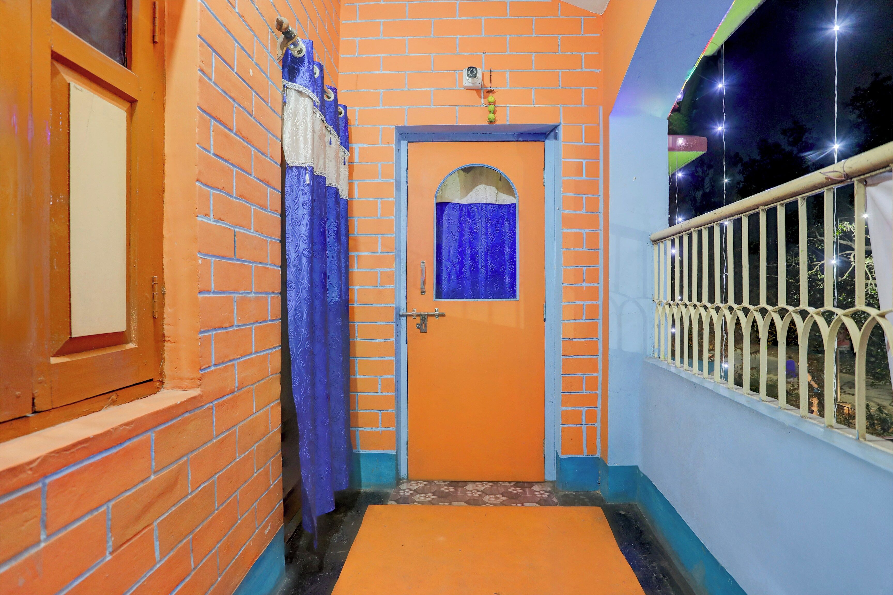 Un pasillo con una puerta naranja, una ventana con cortinas azules y una barandilla metálica a la derecha.