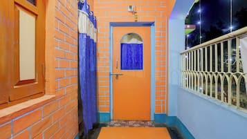 Un pasillo con una puerta naranja, una ventana con cortinas azules y una barandilla metálica a la derecha.
