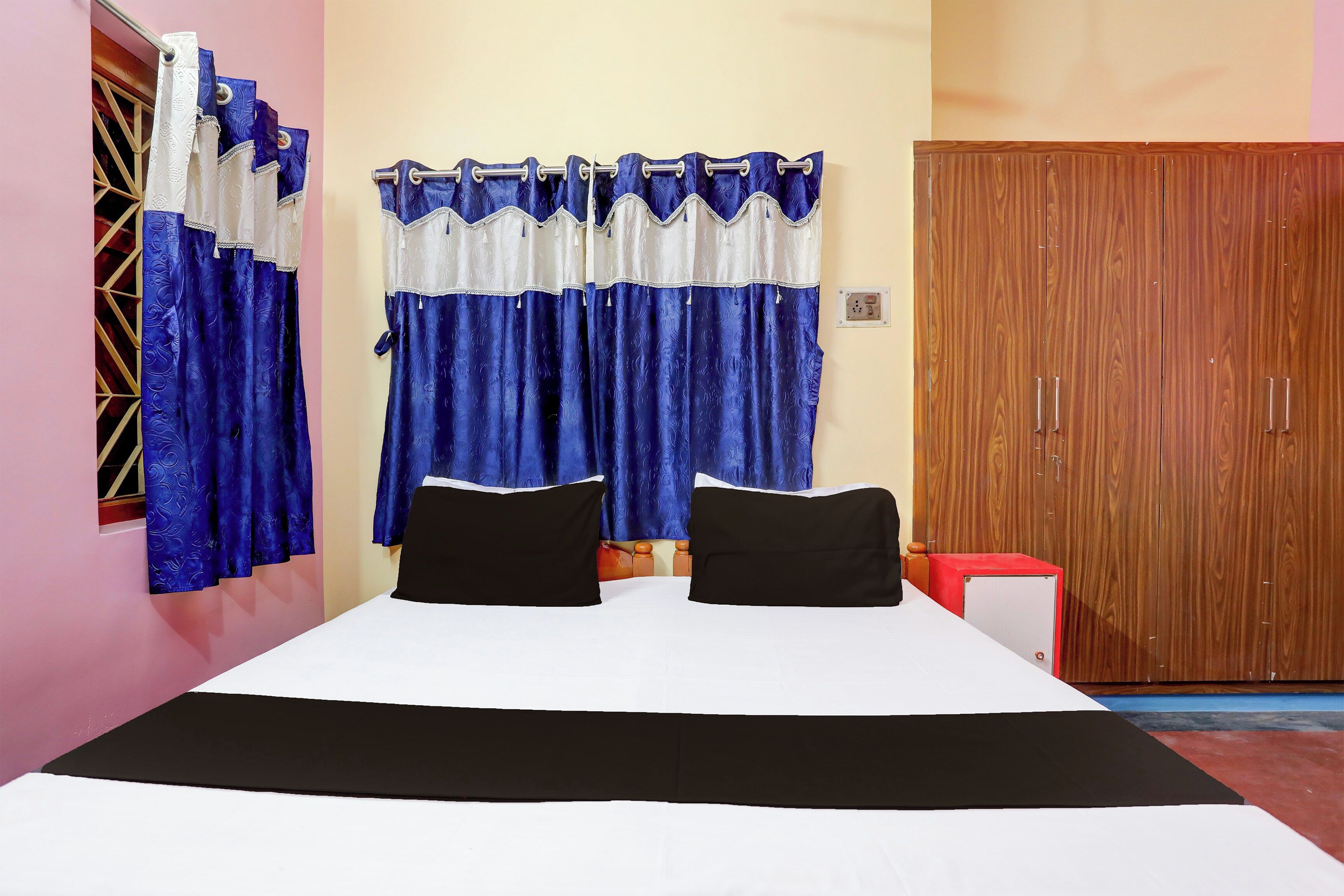 Un dormitorio con una cama, dos almohadas negras, un armario de madera y cortinas azules.