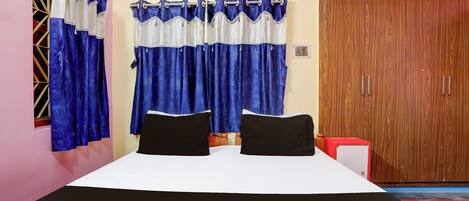 A bedroom with a bed, two black pillows, a wooden wardrobe, and blue curtains.