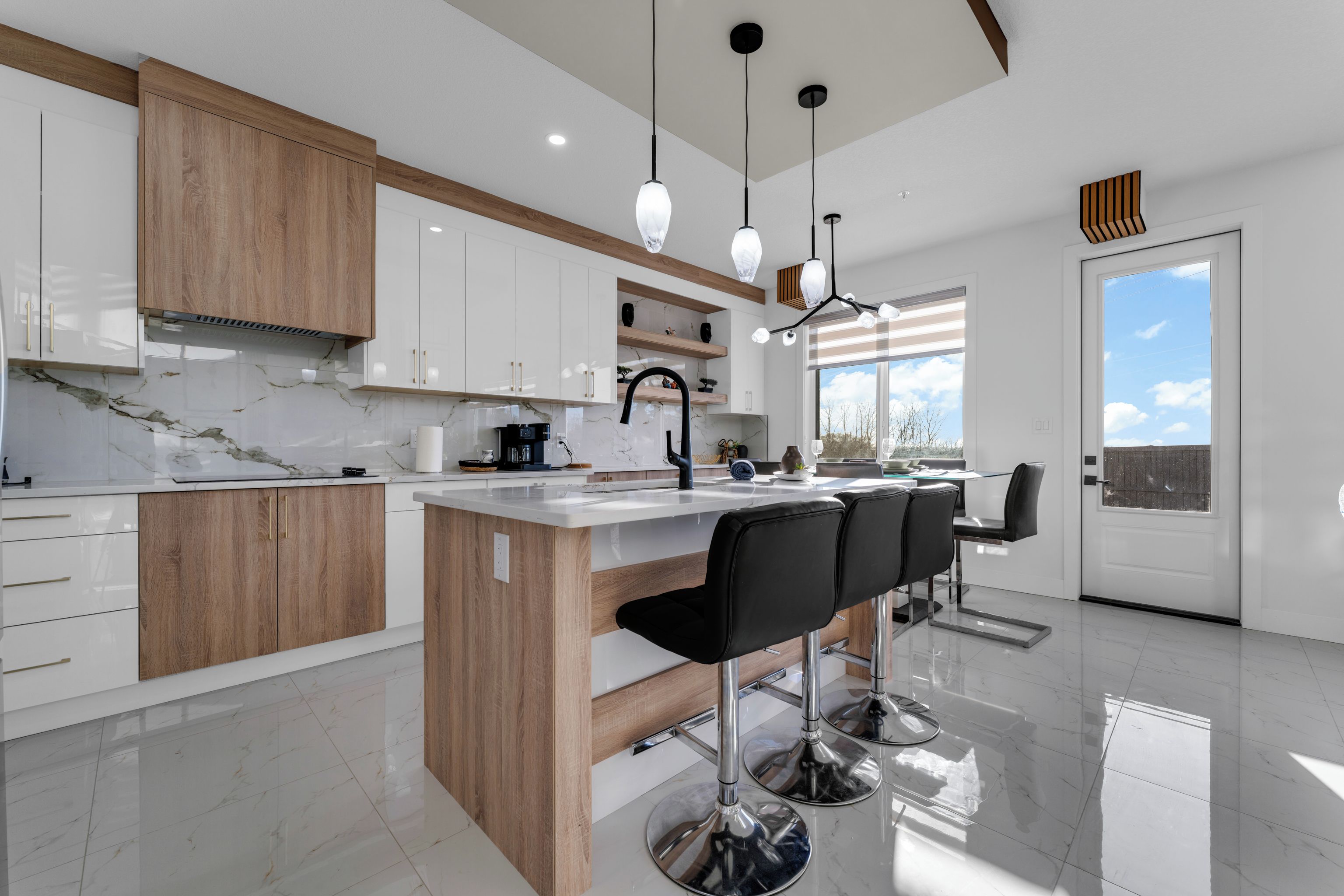 Een moderne keuken met een marmeren aanrecht, houten kastjes en een centraal eiland met barstoelen.