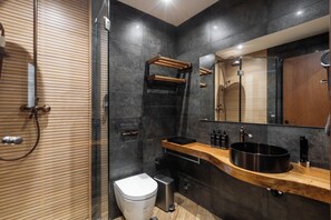 Ein modernes Badezimmer mit einem Holzwaschtisch, einem großen Spiegel und einem schwarzen Waschbecken.