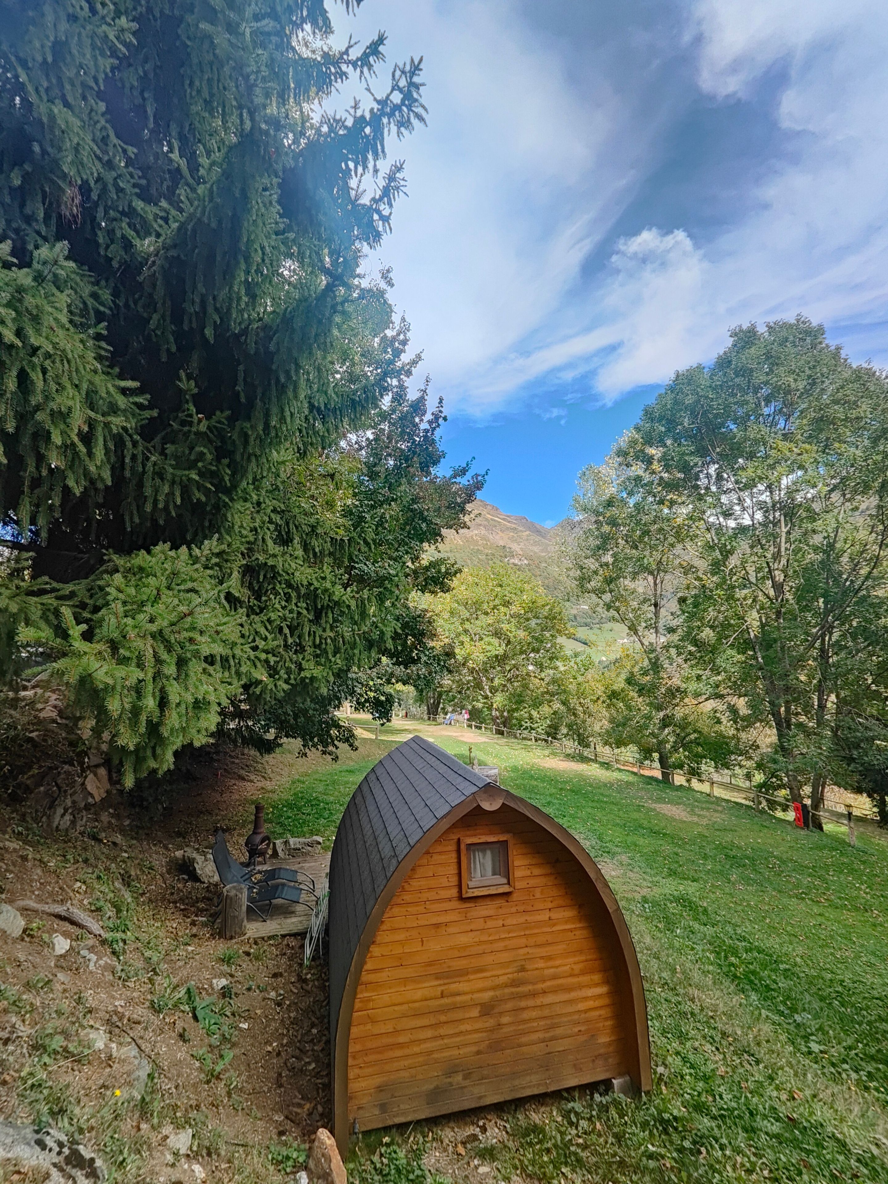 Una cabaña de madera con techo inclinado, rodeada de césped y árboles.