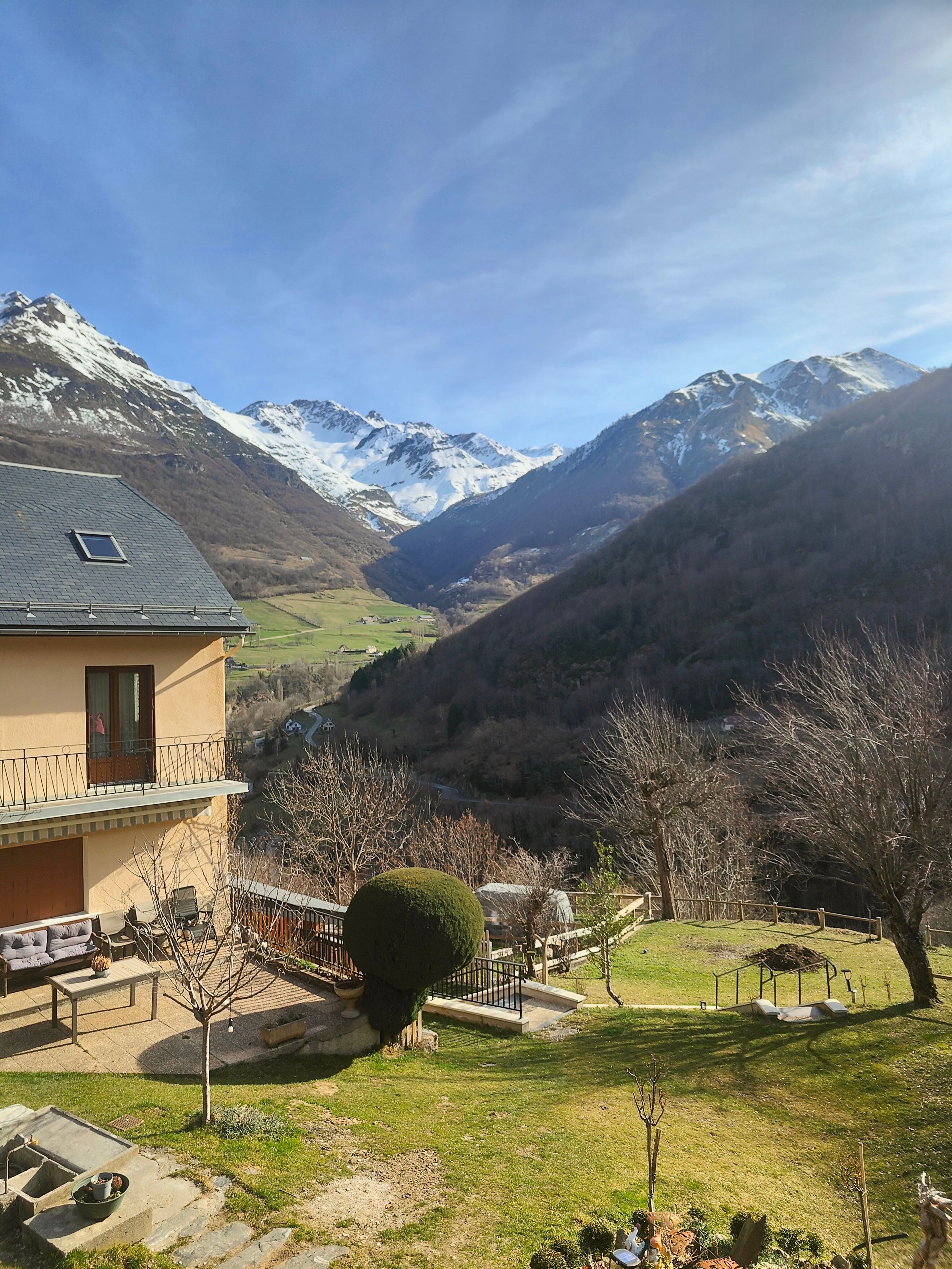 A building with a balcony, a small garden, and a view of snow-capped mountains.