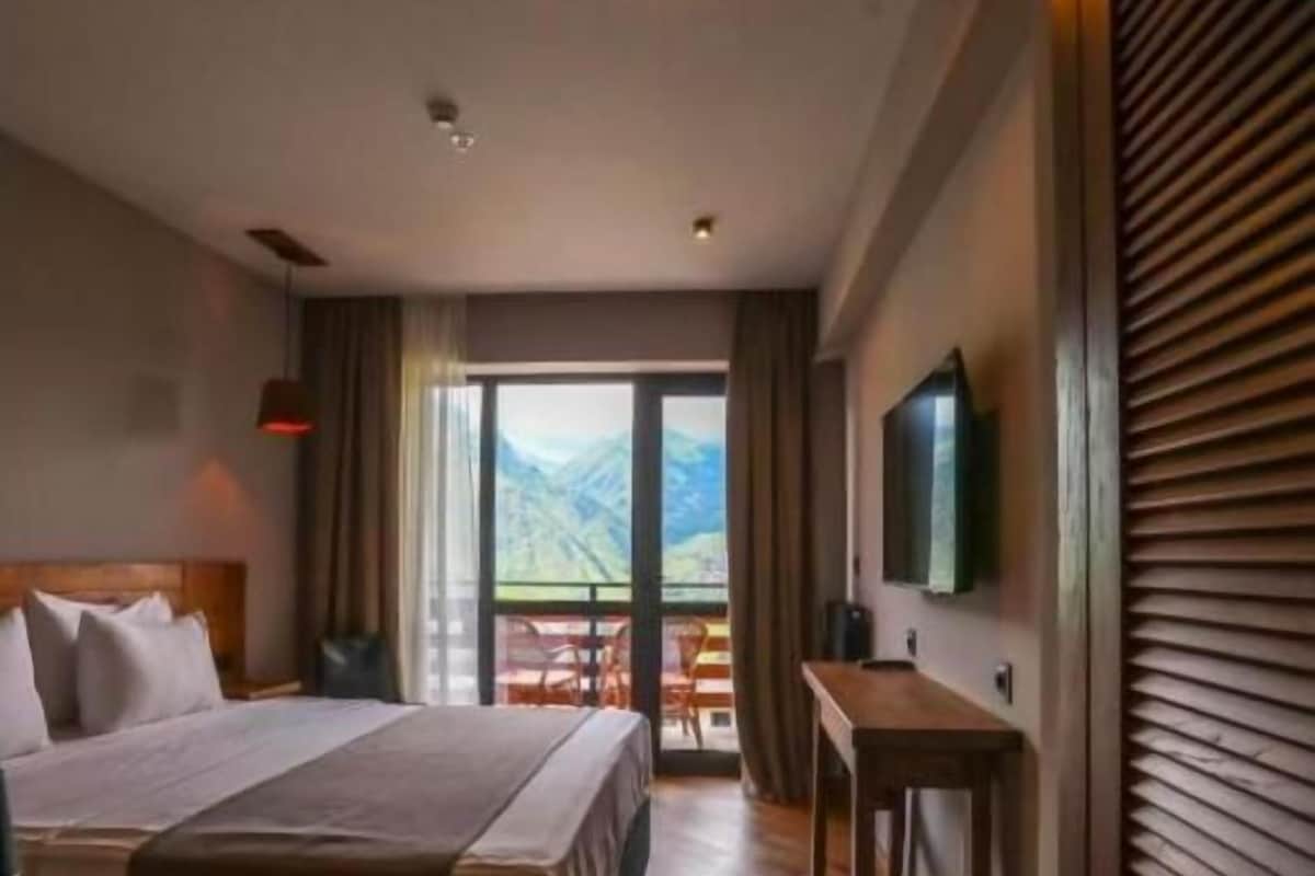 A hotel room with a bed, a desk, and a view of mountains through the window.