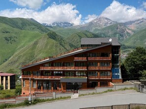 A modern multi-story building with a balcony, set against a mountainous backdrop. - Lens Design Hotel (Stepantsminda)