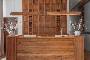 A wooden reception desk with a built-in sink, flanked by wooden paneling and two potted plants. - Lens Design Hotel (Stepantsminda)