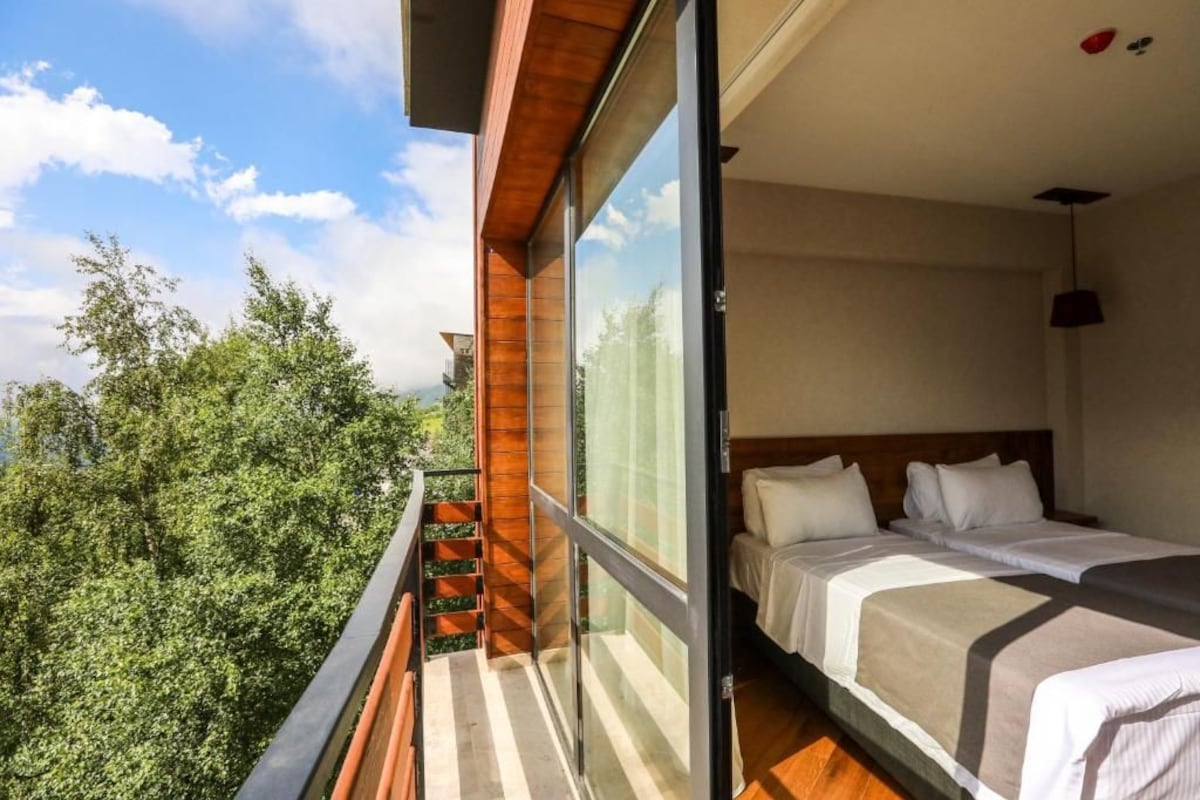 A bedroom with a large window, a bed, and a view of trees.