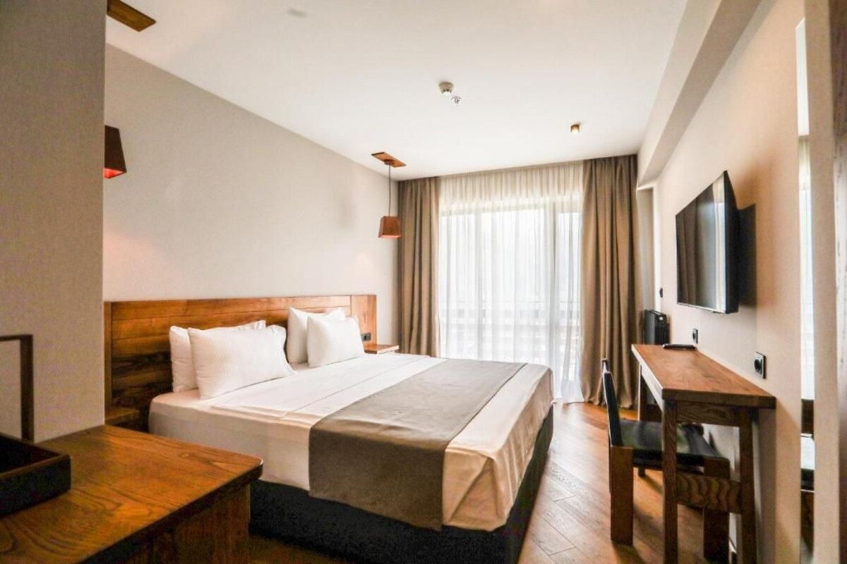 A hotel room with a bed, a desk, a chair, a television, and a window with curtains.