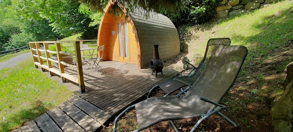 A wooden deck leading to a small cabin with a heart-shaped window, a metal chair, and a stone wall in the background. - Cabin 'Gavarnie, Sanitaire Camping' with Mountain View, Private Terrace and Wi-Fi (Gavarnie-Gèdre)