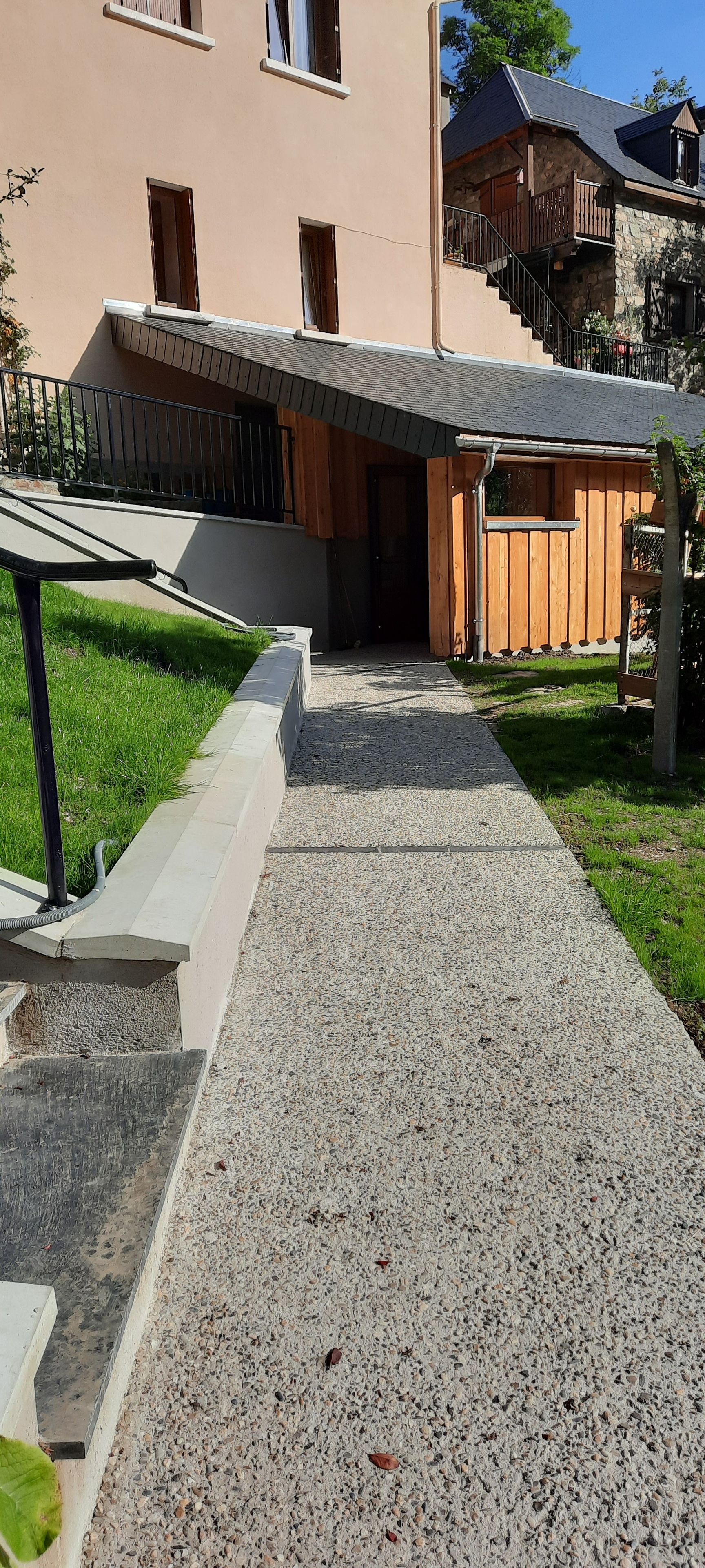 A pathway leading to a building with a stone facade and a wooden deck.