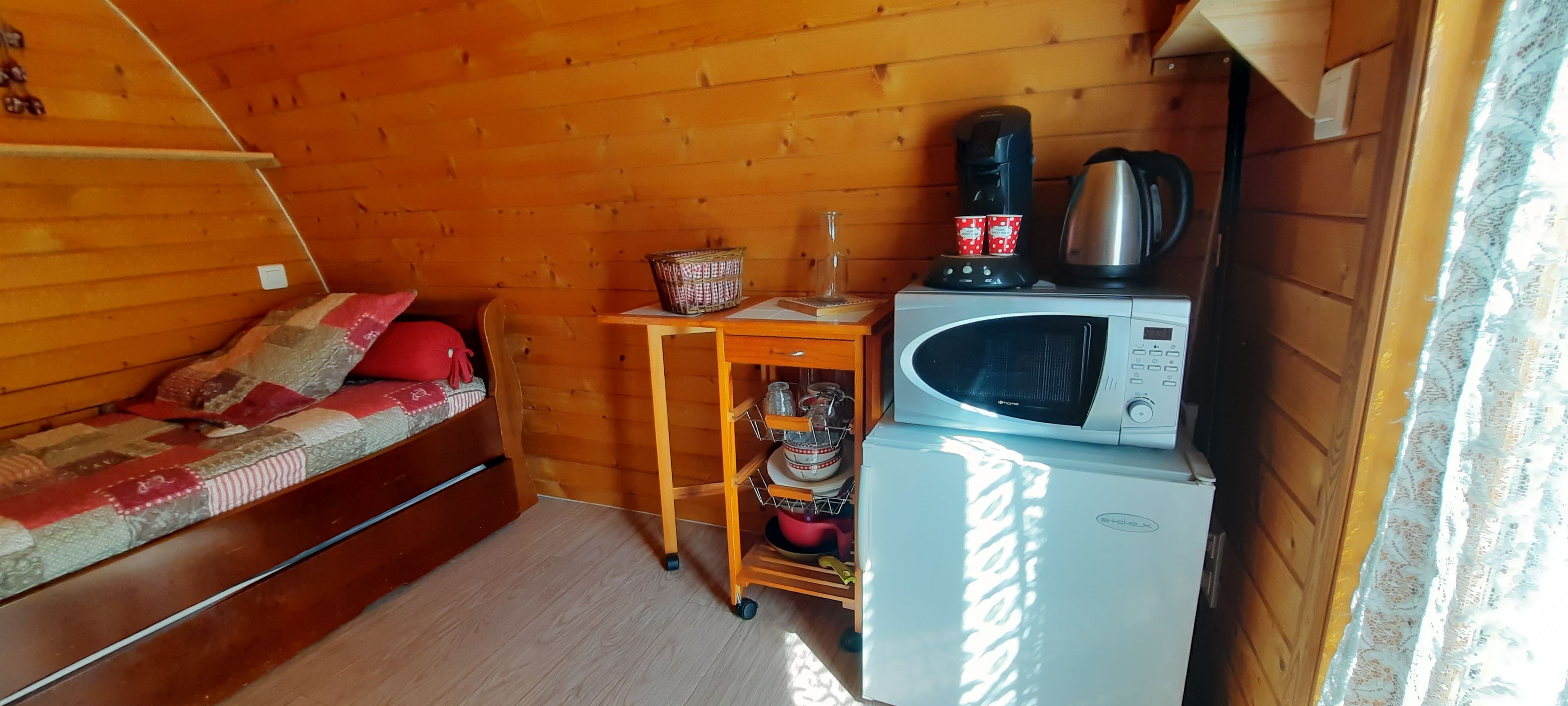A compact room with a bed, a small table with a kettle, a microwave, and a refrigerator.
