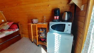 A compact room with a bed, a small table with a kettle, a microwave, and a refrigerator.