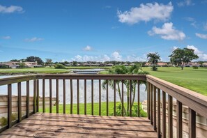 Una terraza de madera con vista a un campo de golf, un cuerpo de agua y casas a lo lejos.
