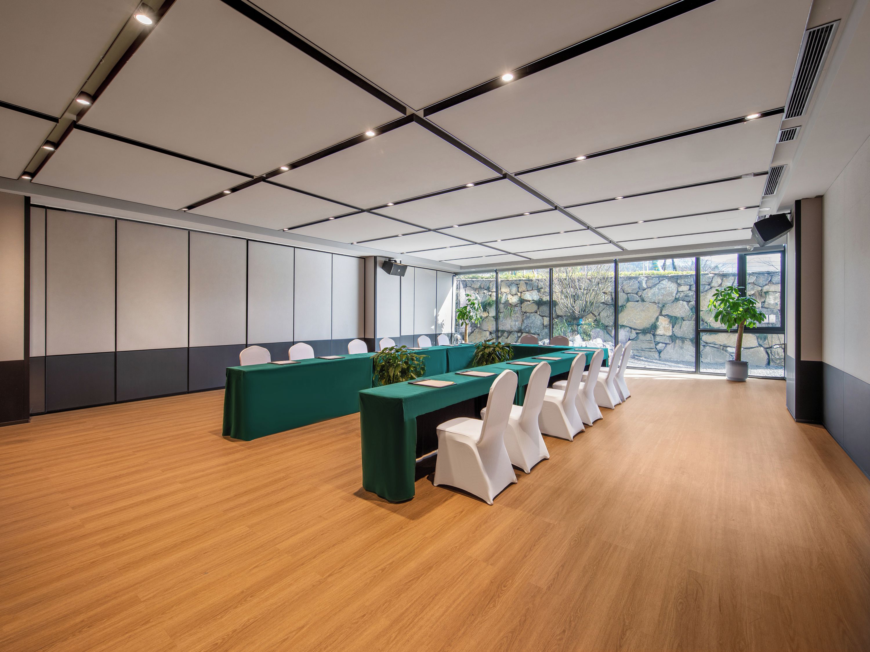 Un salón de conferencias con una larga mesa, sillas blancas y una planta en maceta.