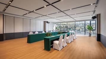 Un salón de conferencias con una larga mesa, sillas blancas y una planta en maceta.