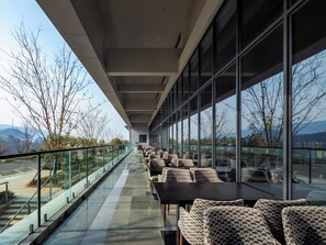 Un área de estar moderna al aire libre, con barandillas de vidrio, sillas estampadas y vistas al paisaje.