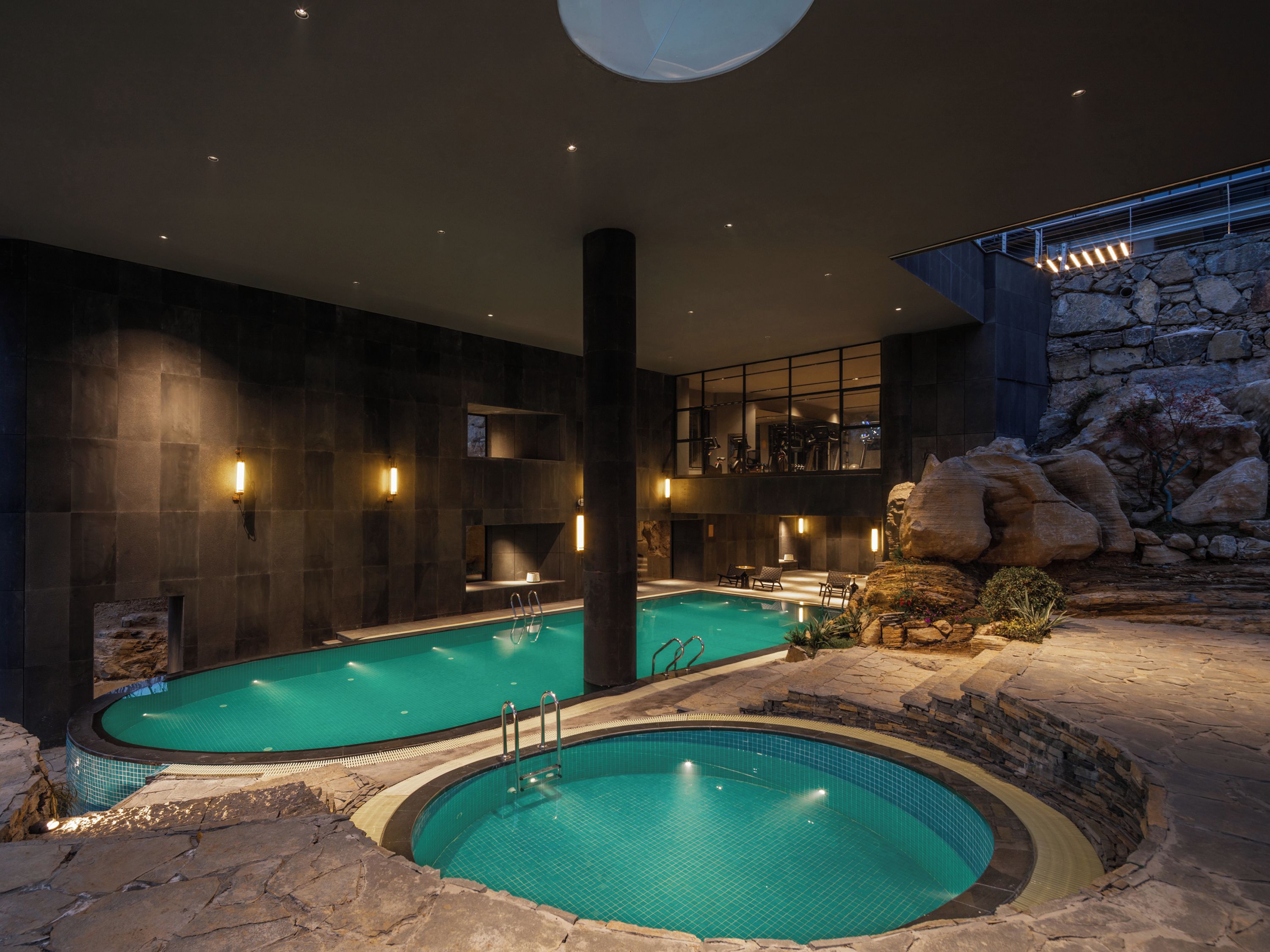 An indoor swimming pool with a stone wall and a view of the sky.