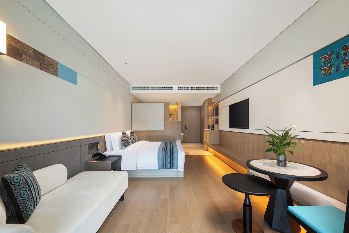 Una habitación de hotel moderna con una cama, un sofá, una mesita y un televisor.