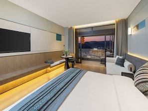 Una habitación de hotel moderna con una cama grande, una zona de estar con vistas y una mesa de comedor.