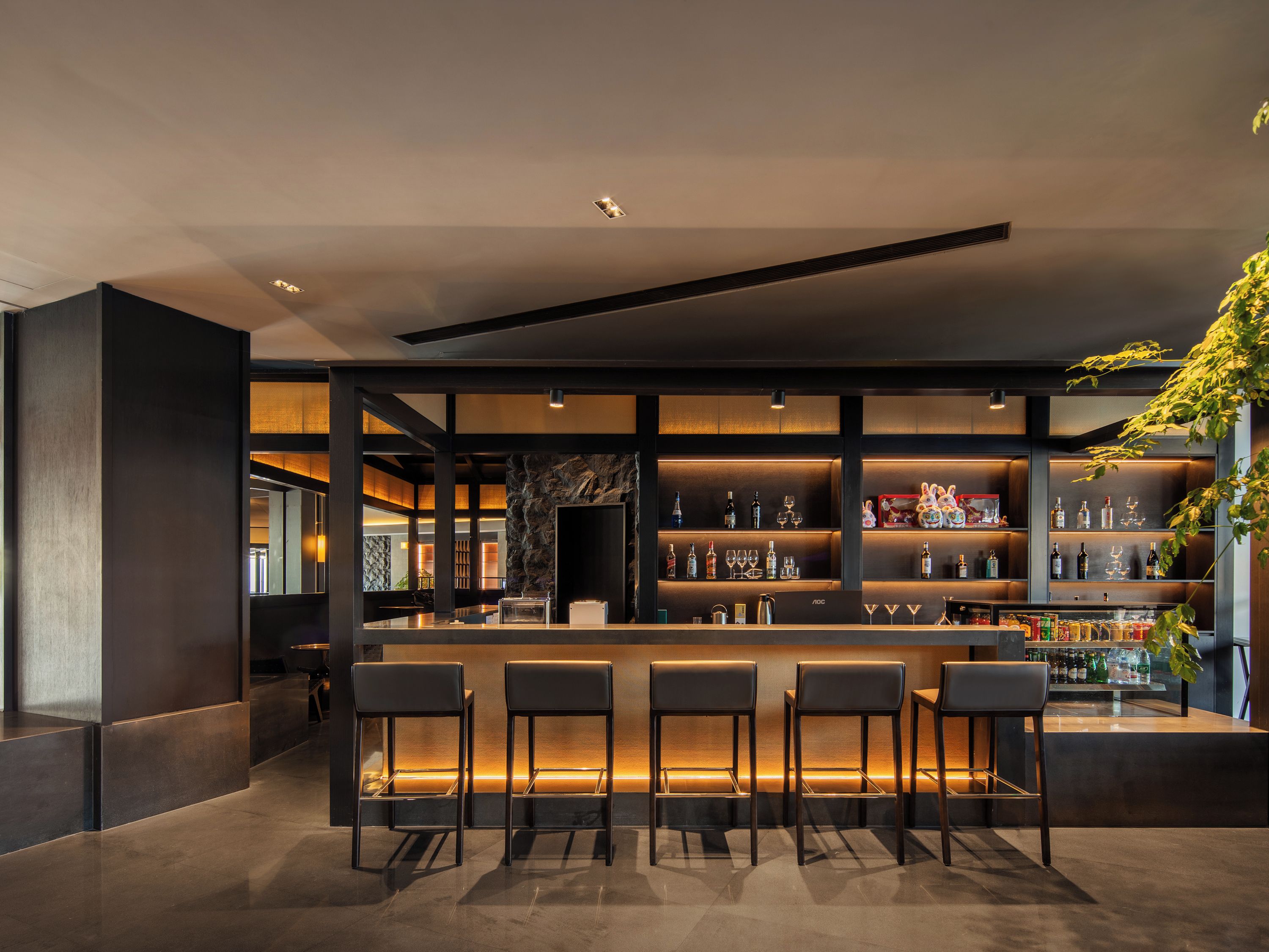 A modern bar area with a long counter, multiple shelves of bottles, and bar stools.