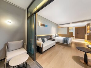 Una habitación de hotel moderna con sofá, una mesita redonda, una cama con cabecera y un espejo grande.