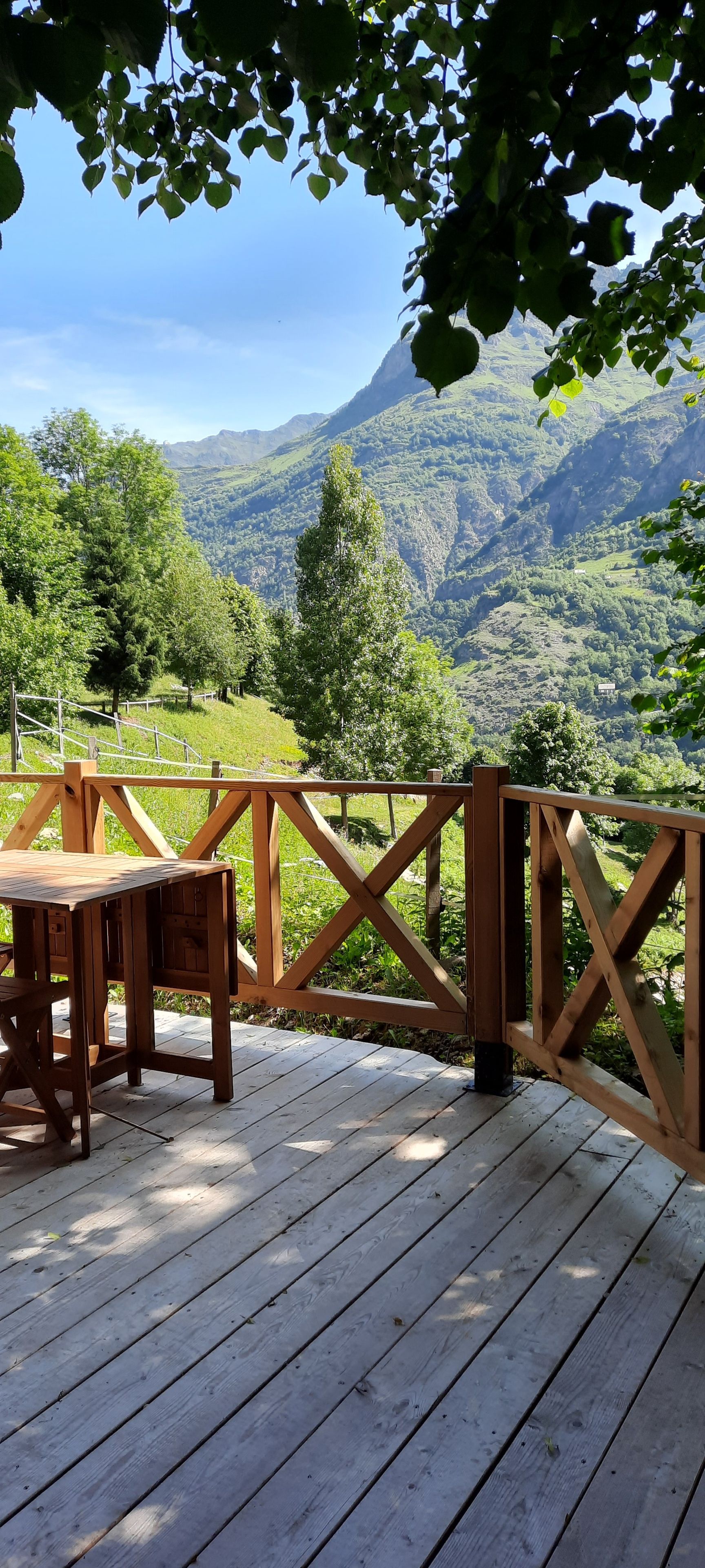 Una terraza de madera con una mesa y sillas, con vistas a un paisaje montañoso.
