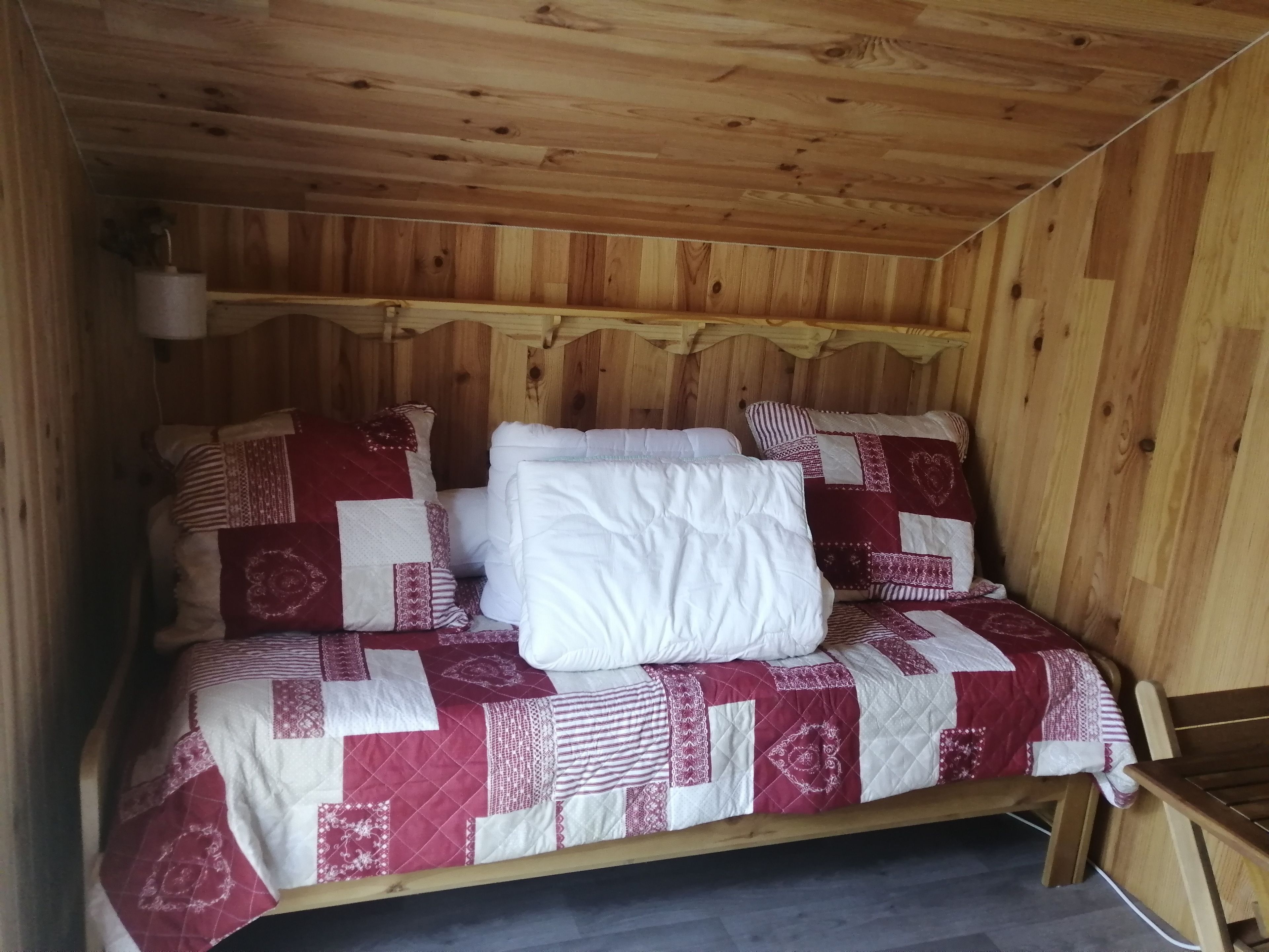 Habitación de cabaña de madera con una cama que tiene una colcha acolchada roja y blanca y varias almohadas.