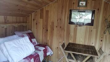 A wooden cabin room with a bed, a small table, and a window with a picture.