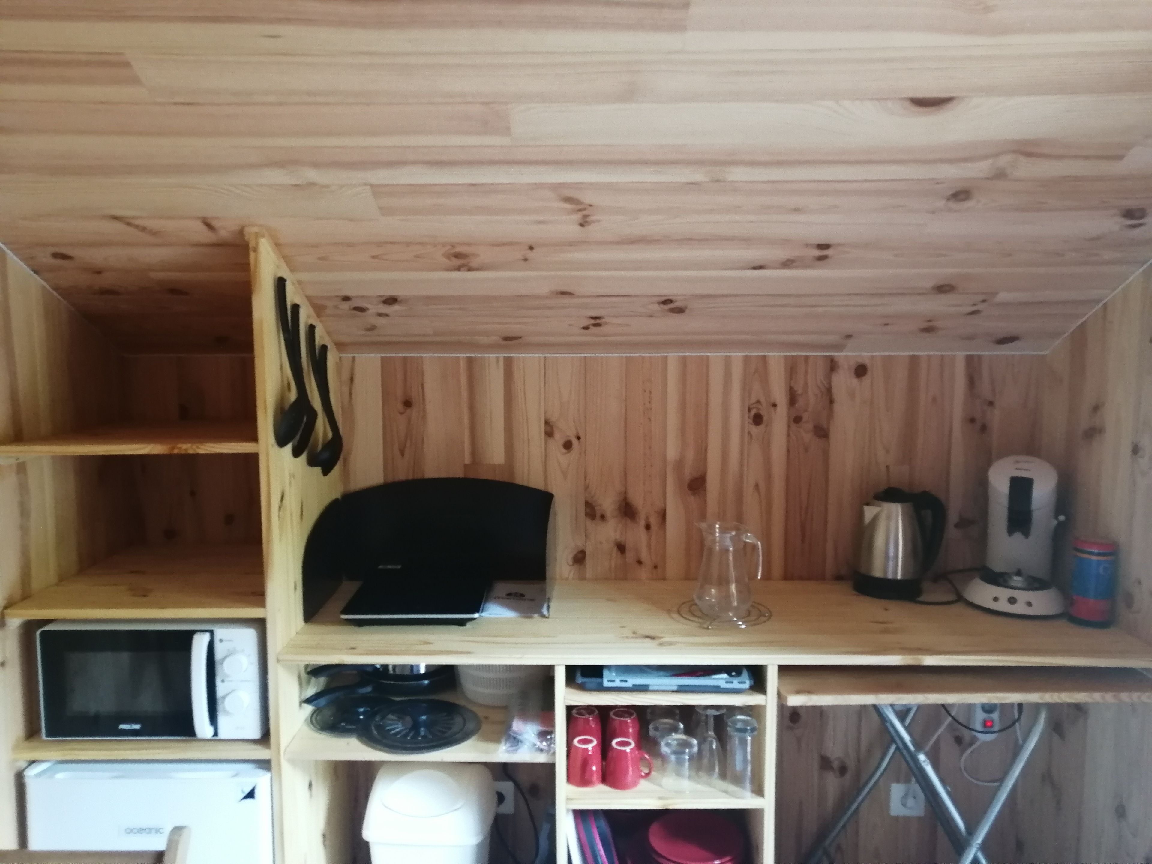 A compact kitchen with wooden walls, a microwave, a kettle, and various kitchen utensils.