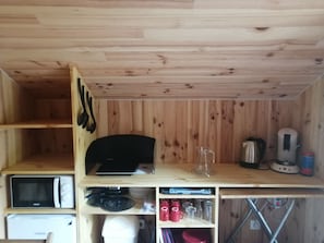 Una cocina compacta con paredes de madera, microondas, hervidor y diversos utensilios de cocina.