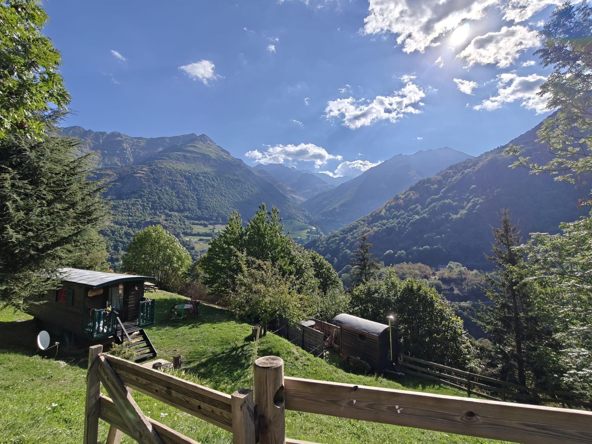Une cabane en bois, dotée d’une antenne parabolique, entourée d’une végétation luxuriante et avec des montagnes en arrière-plan.