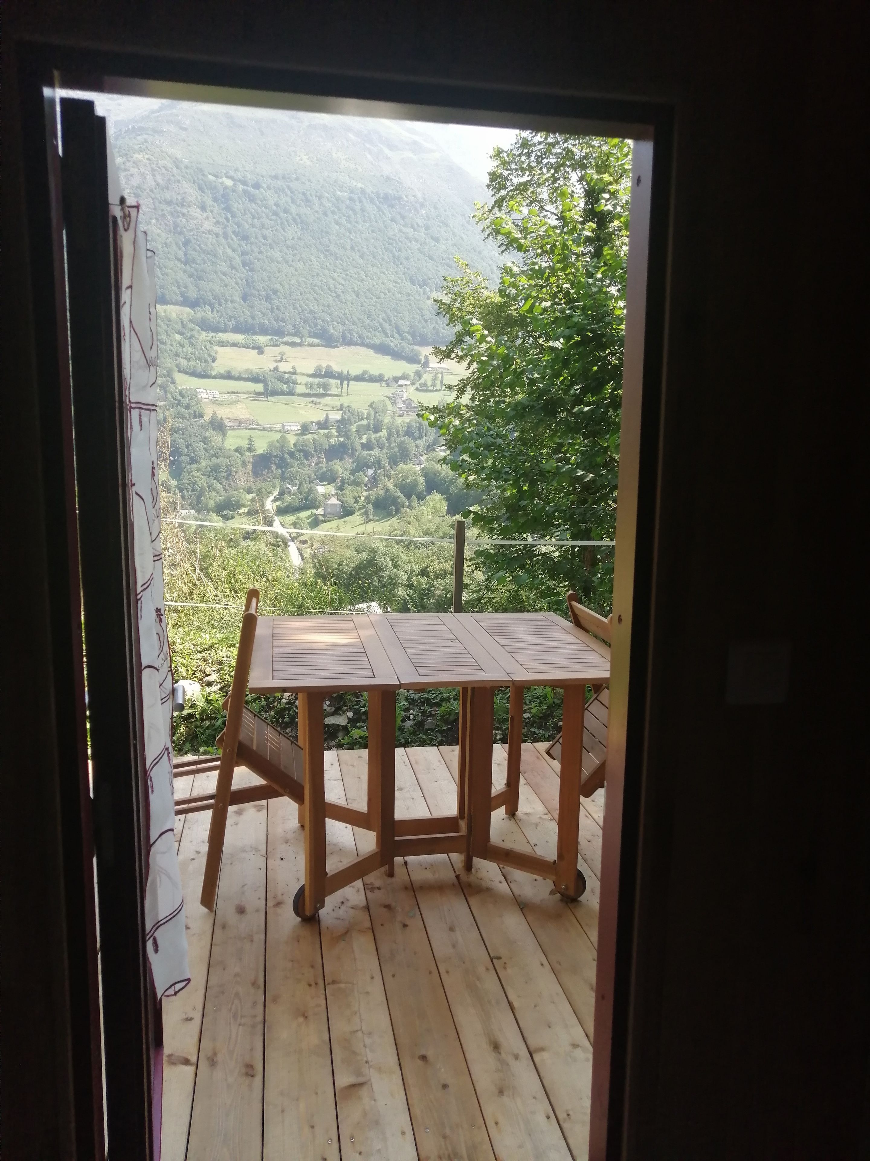 A wooden deck with a table and chairs, overlooking a valley with greenery and buildings.