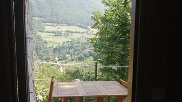 A wooden deck with a table and chairs, overlooking a valley with greenery and buildings.